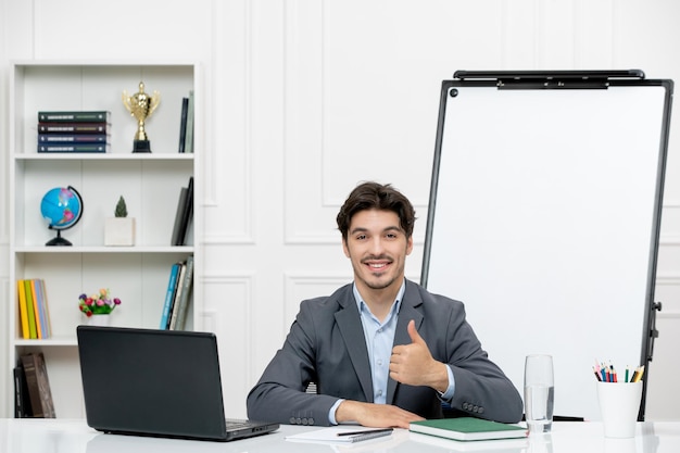 Profesor joven instructor en traje de oficina en la clase con laptop y pizarra sonriendo