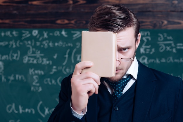 Profesor joven en traje que cubre su rostro con el libro. Closeup retrato de joven profesor.