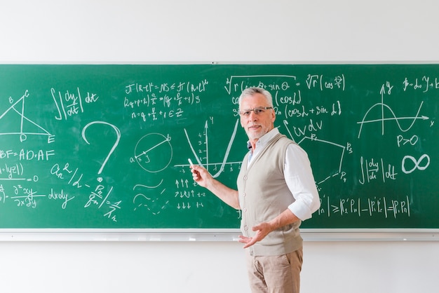 Foto profesor de matemáticas envejecido que señala con tiza en la pizarra