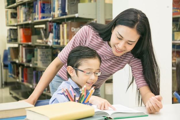 Profesor de mujer y niño estudiante aprenden con el libro en el fondo del estante