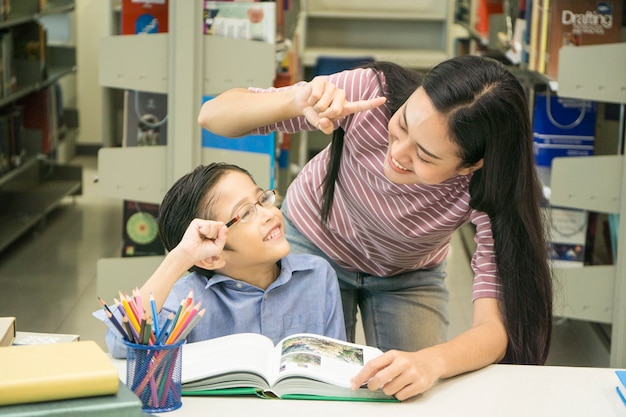 Profesor de mujer y niño estudiante aprenden con el libro en el fondo del estante