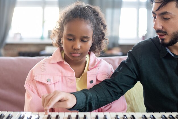 Foto profesor de música presionando la tecla del teclado del piano mientras consulta a un estudiante birracial