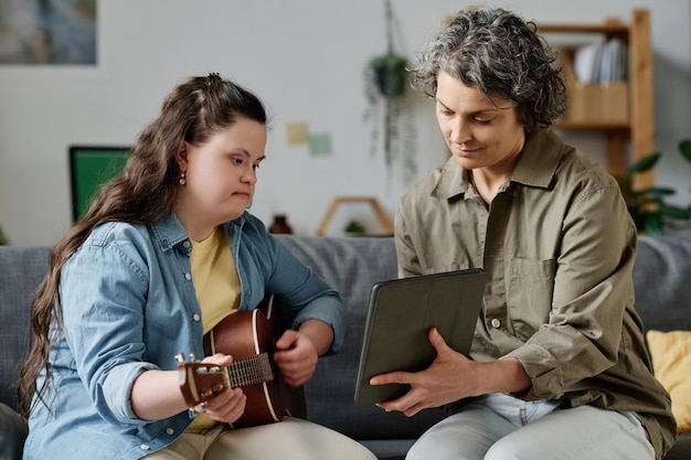 Profesor de música usando tablet pc mientras tiene una lección con una niña con síndrome de down