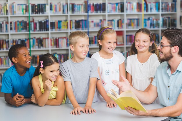 Profesor y niños leyendo el libro en la biblioteca