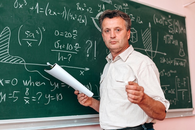 Profesor de pie junto a una pizarra y explicar una lección con un libro de texto.