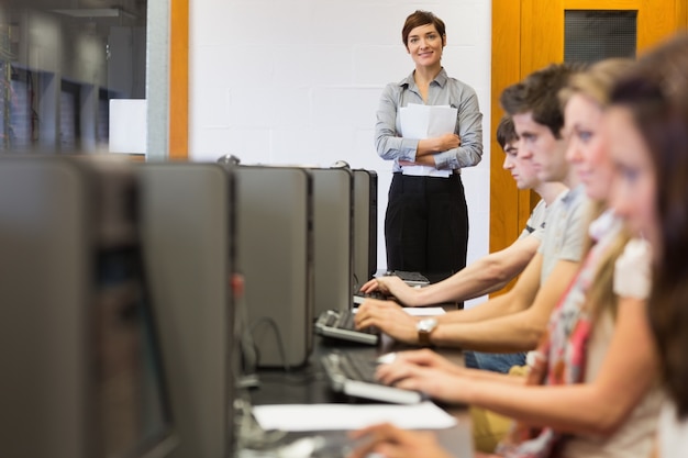 Profesor de pie mientras los estudiantes sentados en la computadora