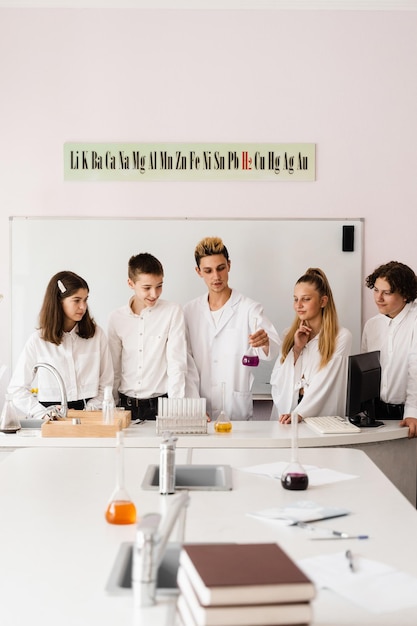 El profesor de química escolar muestra a los niños frascos con líquidos para experimentos en el laboratorio Concepto de educación Lección grupal de compañeros de clase en la lección de química