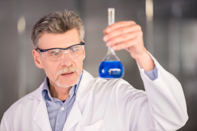 Foto profesor de química superior que sostiene el frasco con líquido azul.