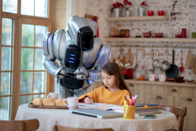 Profesor robot mirando atentamente cómo la niña escribe