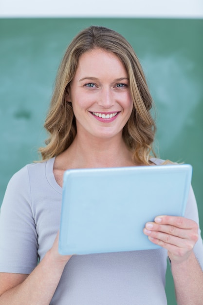 Profesor sonriente que sostiene la PC de la tableta delante de la pizarra