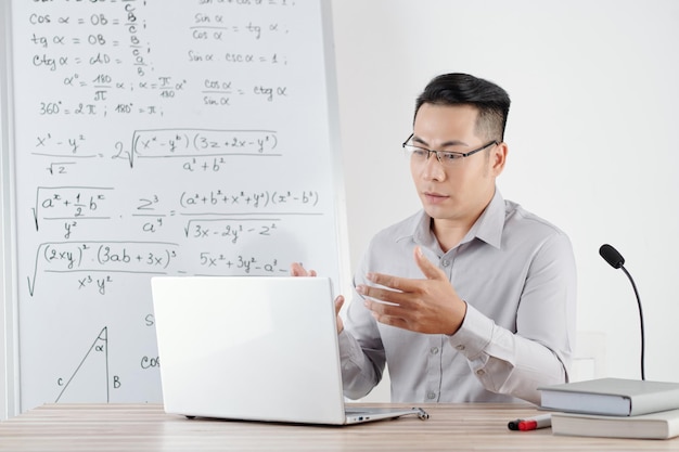 Profesor universitario sentado en el escritorio con una computadora portátil abierta y grabando clases en línea para estudiantes