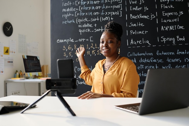 Profesora afroamericana liderando su blog en línea sobre esto mientras está sentada en la mesa frente a smartph