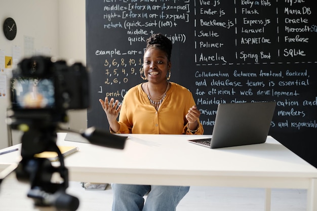 Profesora afroamericana sentada en la mesa frente a la cámara y grabando su blog al respecto