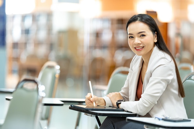 Profesora de Asia tomando notas de la tableta en la biblioteca de la universidad