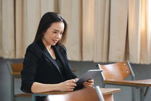 Una profesora asiática de mediana edad sosteniendo una tableta sentada en el aula de la Universidad