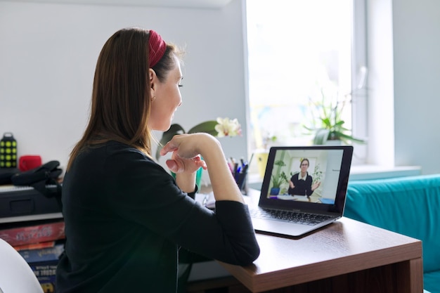 Profesora enseñando a una estudiante adolescente en línea usando una videollamada en una computadora portátil