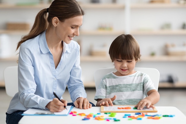 Profesora de idiomas profesional haciendo ejercicio con un niño en edad preescolar haciendo palabras con letras