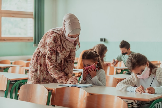 Profesora con máscara médica señalando con un dedo cerca de una colegiala aburrida Nueva educación normal durante la pandemia de Covid19 Enfoque selectivo Foto de alta calidad