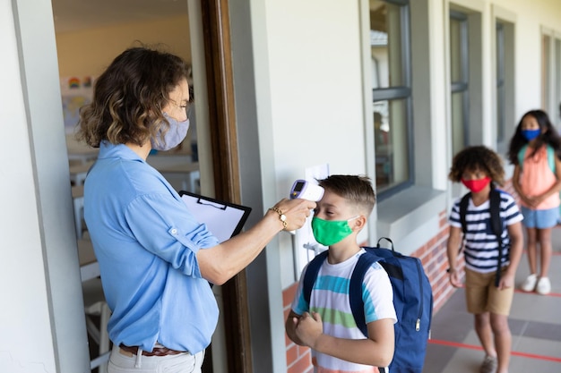 Foto profesora con mascarilla midiendo la temperatura de un niño