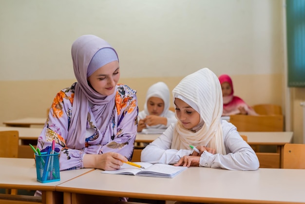 La profesora musulmana hijab ayuda a los escolares a terminar la lección en el aula.