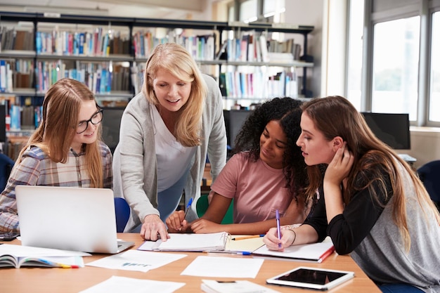 Profesora que trabaja con alumnas universitarias en la biblioteca