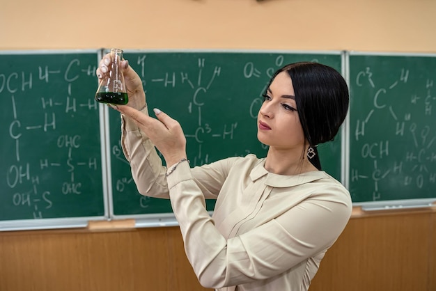 Profesora de química observando el tubo de ensayo de reacción en el aula y contra la pizarra verde