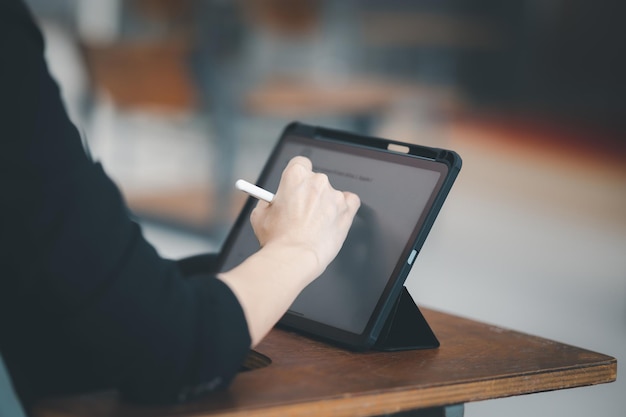 Una profesora con una tableta se sienta en un aula vacía en la universidad. mientras espera para enseñar a los estudiantes en la clase