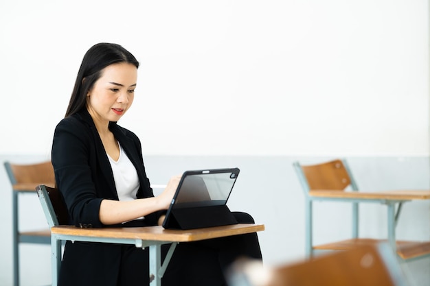 Una profesora con una tableta se sienta en un aula vacía en la universidad. mientras espera para enseñar a los estudiantes en la clase