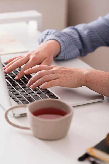 Profesora usando la computadora portátil para escribir durante la clase en línea y tomar el té