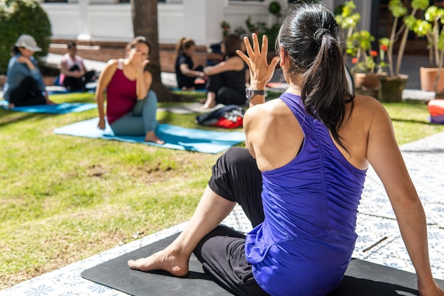 Profesora de yoga por detrás liderando un entrenamiento en un jardín a un grupo de mujeres irreconocibles