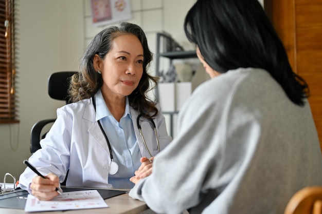 Professionelle ältere asiatische Ärztin trifft sich mit ihrer Patientin im Büro