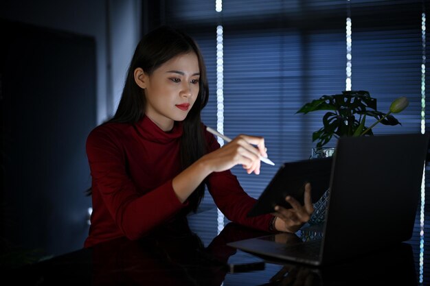 Professionelle asiatische Geschäftsfrau, die sich mit einem Tablet konzentriert und spät im Büro arbeitet