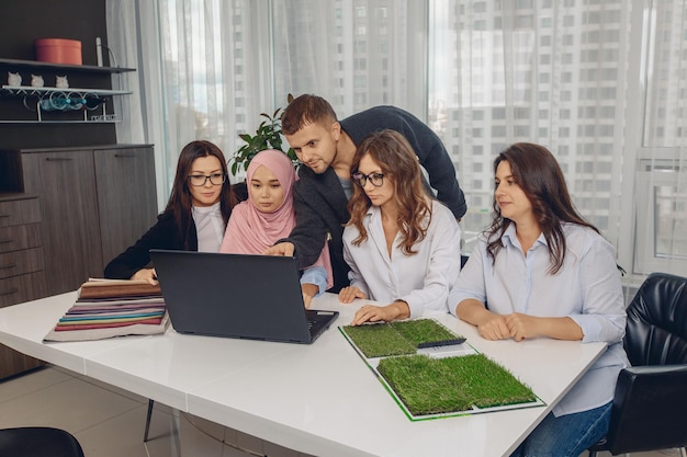Professionelle attraktive Gruppe vielversprechender Büroangestellter, die ein Projekt analysieren und bearbeiten. Schöne Frau in einem rosa Hijab im Büro. Multireligiöses Team. Konzept der Teamarbeit