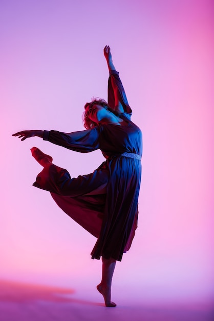 Professionelle Ballerina tanzt Ballett in einem Rauch. Frau im schwarzen Body auf Flutlichthintergrund.