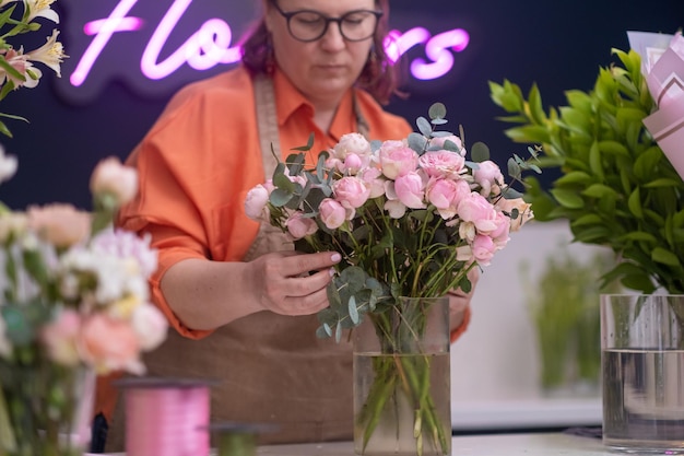 Professionelle Blumendekorateurin Nahaufnahme der Hände einer jungen Floristin, die einen Strauß rosa Rosen kreiert