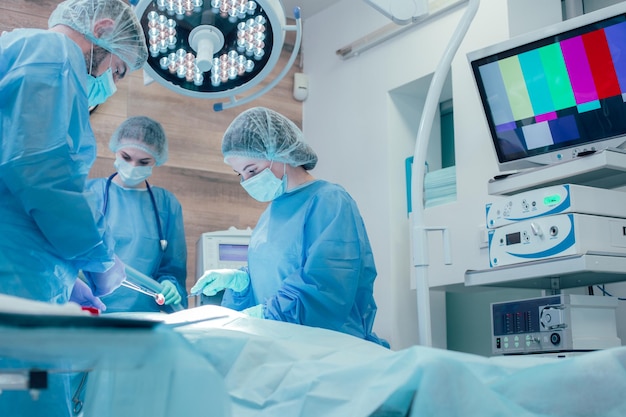 Professionelle Chirurgen in medizinischer Uniform stehen neben dem Patienten im ausgestatteten Operationssaal