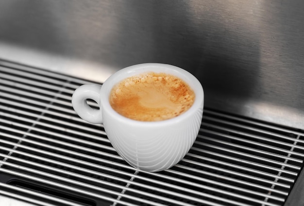 Professionelle Espressomaschine, die stark aussehenden, frischen Kaffee in eine ordentliche Keramiktasse gießt