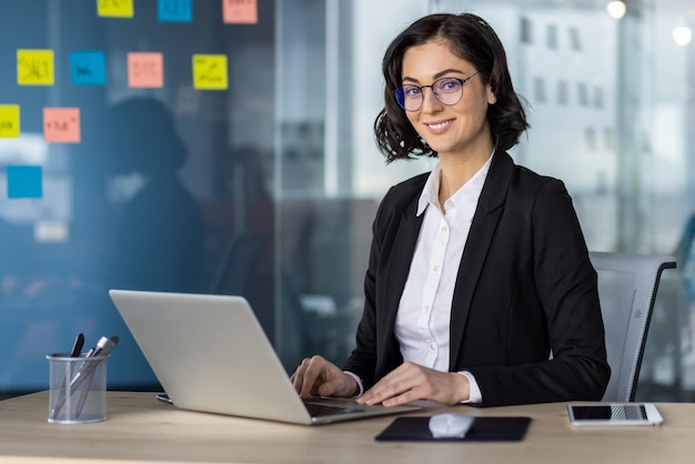 Professionelle Frau arbeitet an einem Laptop in einer modernen Büroumgebung, selbstbewusst und konzentriert.