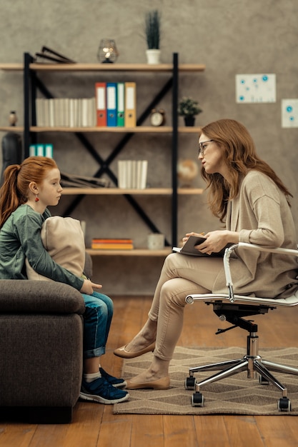 Professionelle Hilfe. Professionelle Psychologin, die ihr Notizbuch hält, während sie ihrem jungen Patienten zuhört