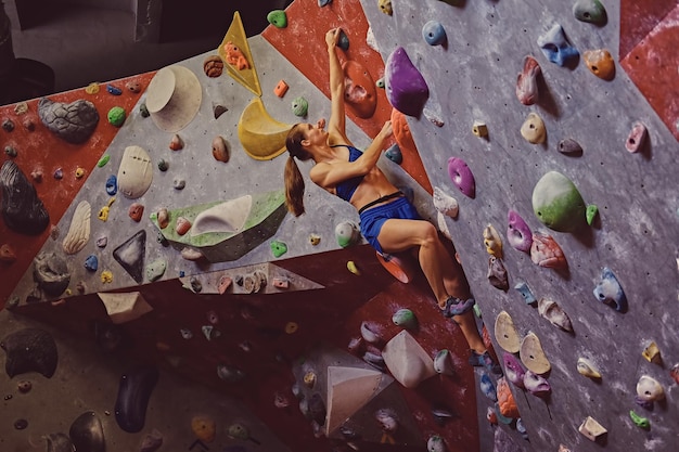 Professionelle Kletterin an einer Boulderwand im Innenbereich.