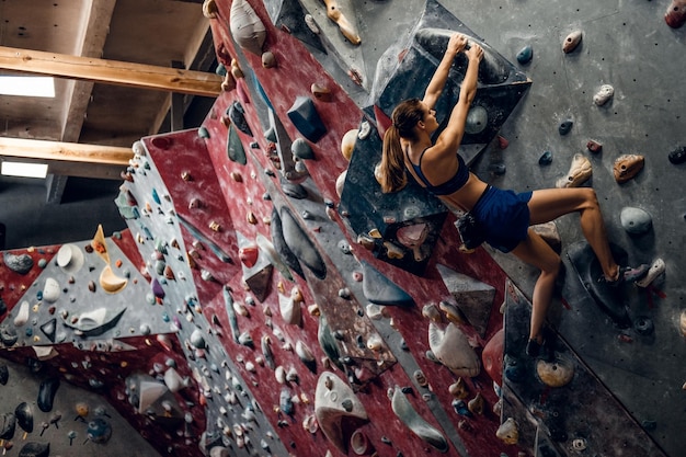 Professionelle Kletterin an einer Boulderwand im Innenbereich.