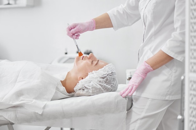 Professionelle Kosmetikerin im Salon bietet umfassende Gesichtspflege für junge Frauen. Porenreinigungsverfahren, Ganzjahrespeeling, straffende Anti-Aging-Maske