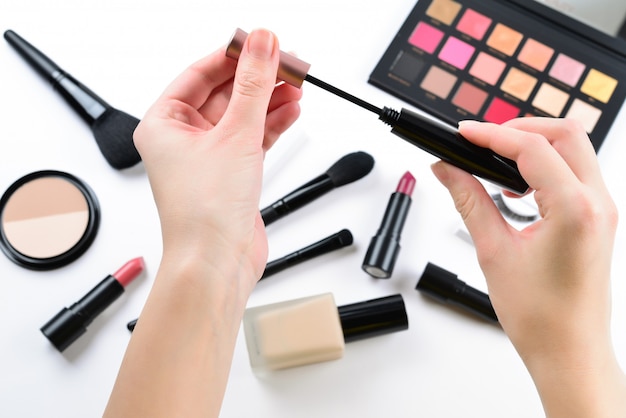 Professionelle Make-up-Produkte mit kosmetischen Schönheitsprodukten, Foundation, Lippenstift, Lidschatten, Wimpern, Pinseln und Werkzeugen. Wimperntusche in Frauenhänden.