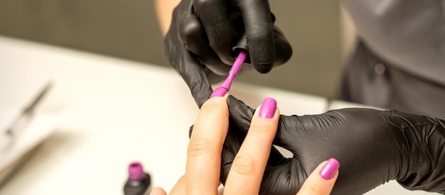 Professionelle Maniküre Ein Manikürist malt die weiblichen Nägel eines Kunden mit violettem Nagellack in einem Schönheitssalon aus nächster Nähe Konzept der Schönheitsindustrie