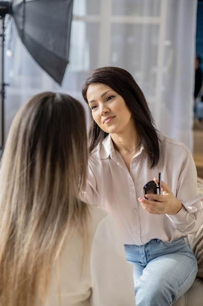 Professionelle Maskenbildnerin, die Kosmetik auf dem Gesicht des Modells aufträgt, verwendet Pinsel, die im Schönheitssalon arbeiten