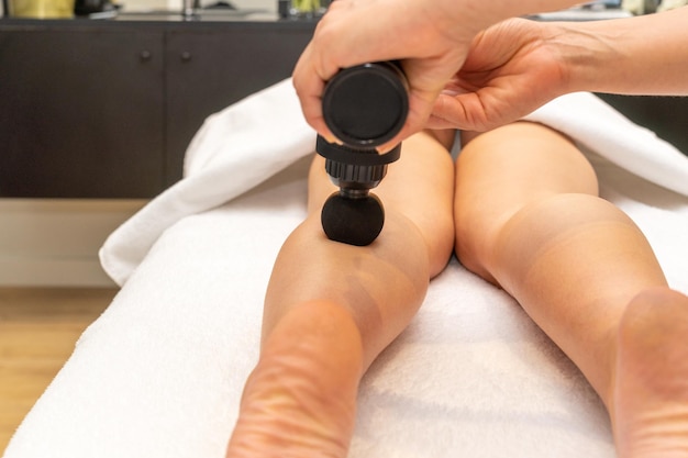 Professionelle Masseurin massiert die Wadenmuskulatur des Beins einer Frau mit der Massagepistole