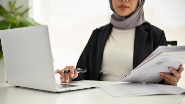 Professionelle muslimische Geschäftsfrau mit Laptop, die Daten analysiert, die in ihrem Büro arbeiten