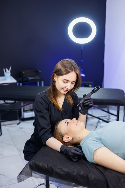 Professionelle Permanent-Make-up-Künstlerin mit einem Permanent-Make-up-Werkzeug. Eine junge Permanent-Make-up-Künstlerin macht permanentes Augenbrauen-Make-up