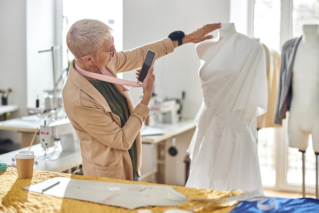 Professionelle Schneiderin fotografiert Schaufensterpuppe, die in der Werkstatt mit weißem Stoff umwickelt ist