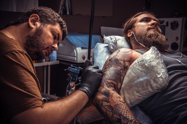 Professionelle Tätowierer erstellen Tätowierungen im Tattoo-Salon. / Mann, der Handschuhe trägt, tätowiert im Salon.